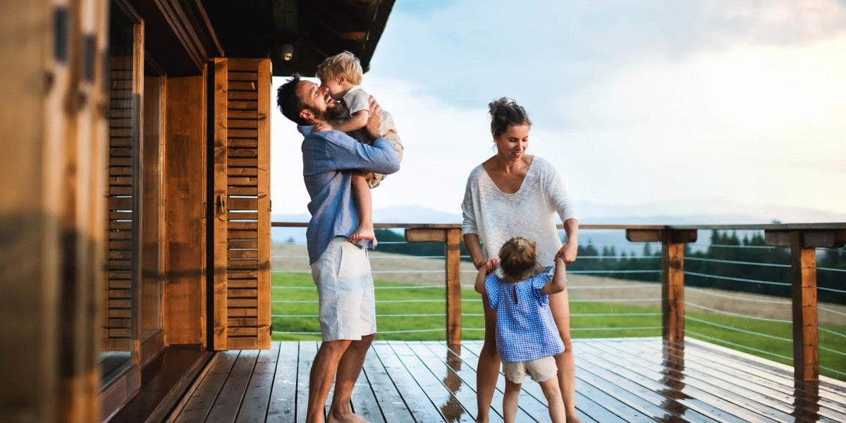 Family with small children playing in rain on patio by wooden cabin.