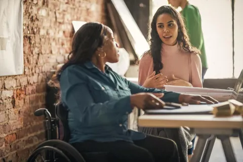 Two women sitting at a table discussing talent attraction and retention strategies.