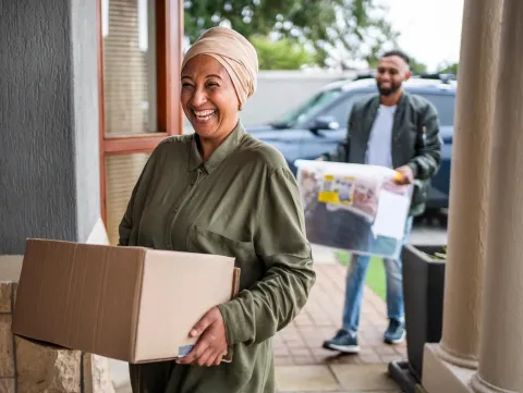 Two people carrying moving boxes into a new home