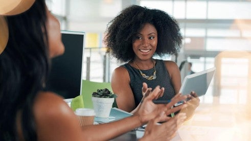 A happy, smiling person checks their tablet while working with a colleague. A happy, smiling person checks their tablet while working with a colleague.