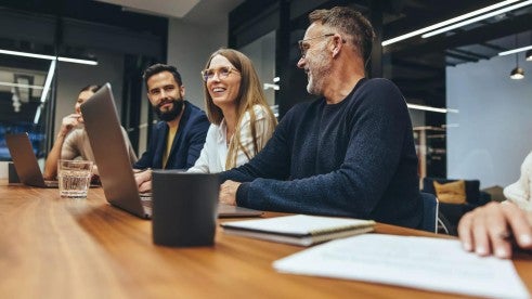 An employee is recognized during a team meeting while the rest of the team at the table nods approvingly in the background. An employee is recognized during a team meeting while the rest of the team at the table nods approvingly in the background.