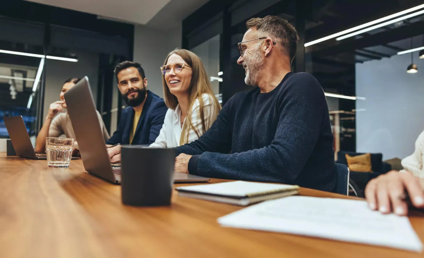 An employee is recognized during a team meeting while the rest of the team at the table nods approvingly in the background.