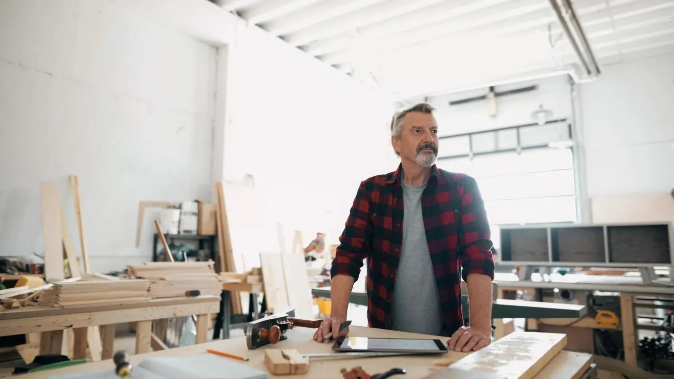 A business owner stands in his workshop and uses a computer tablet to make plans.