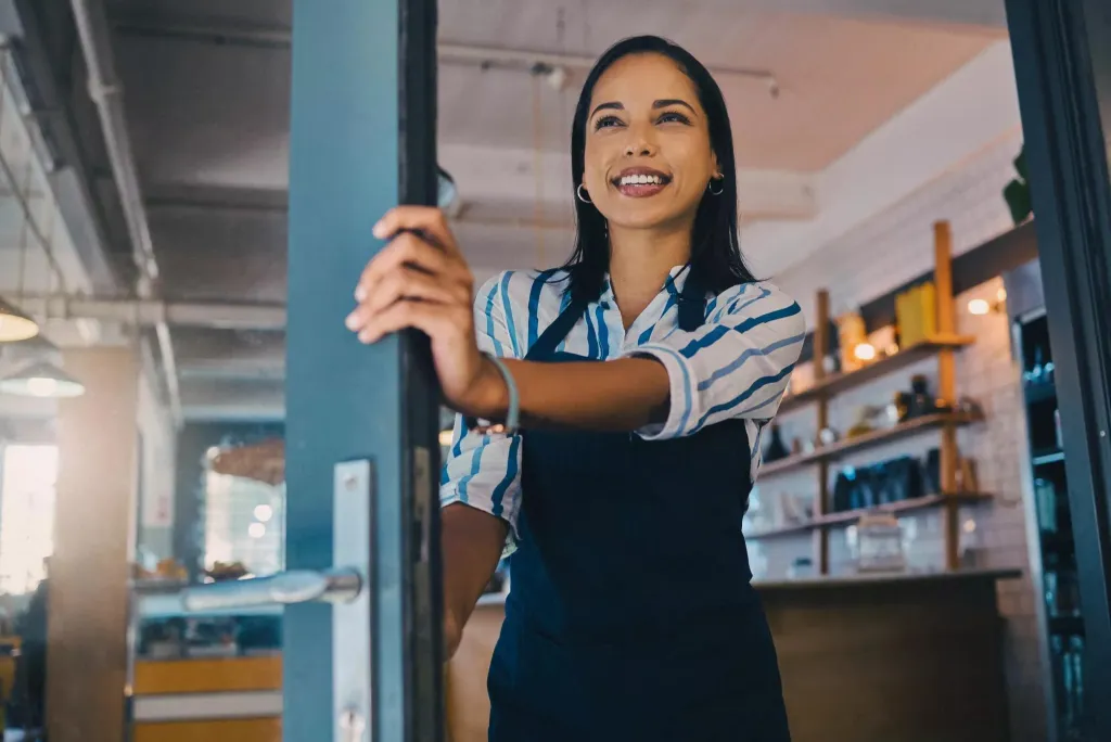 Woman holding open the front door of her business.
