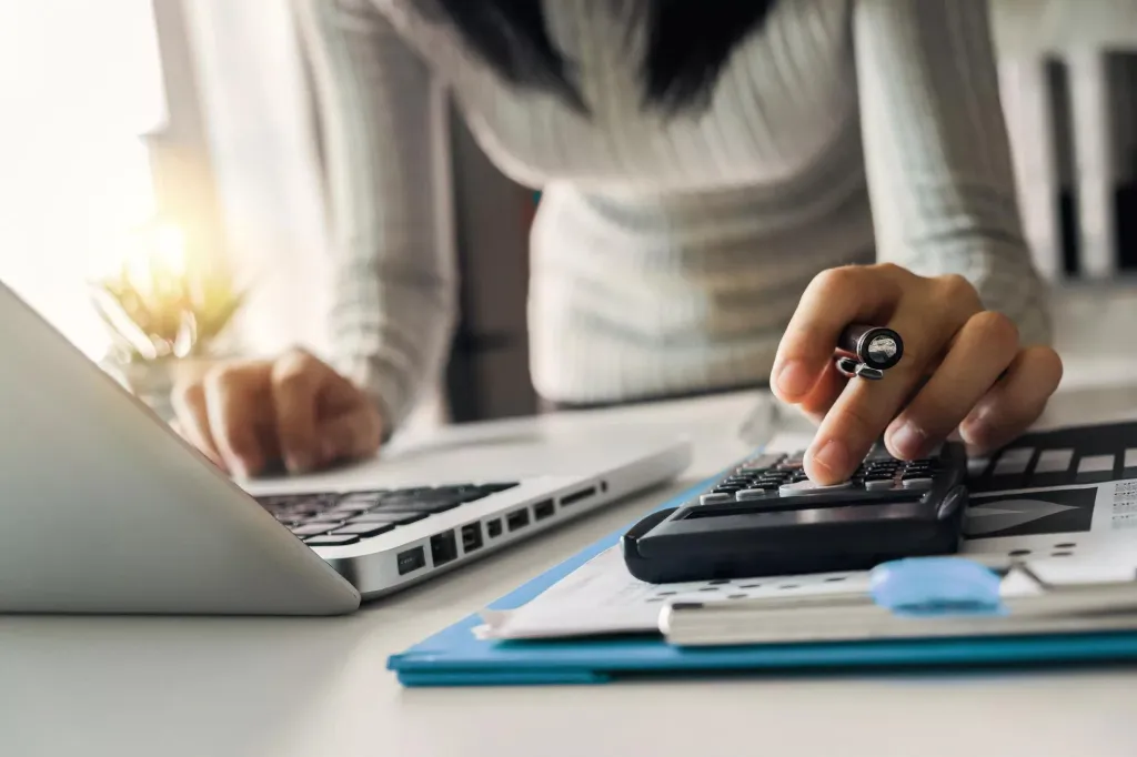 A woman calculating figures and working on a computer.