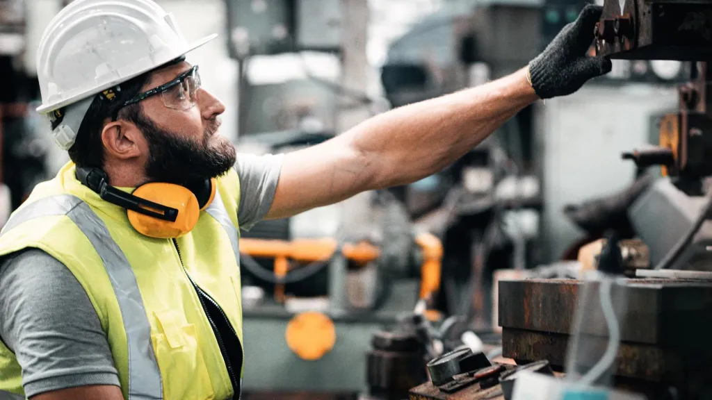 Industrial worker wearing a hard hat, working at a machine.