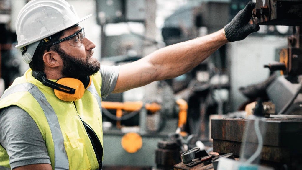 Industrial worker wearing a hard hat, working at a machine. Industrial worker wearing a hard hat, working at a machine.