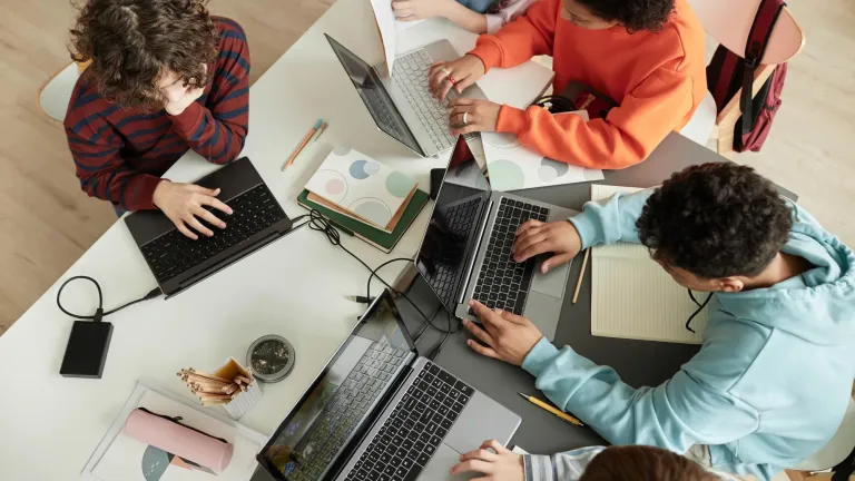 Students gathered around a table working on laptops.
