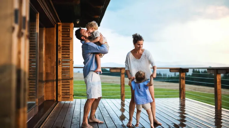 Family with small children playing in rain on patio by wooden cabin.