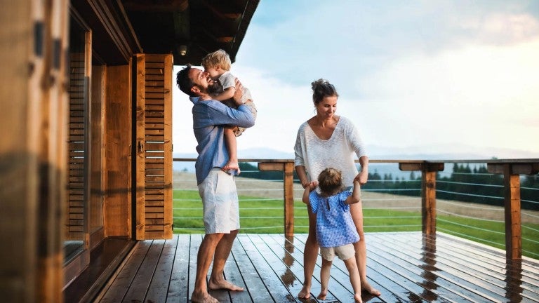 Family with small children playing in rain on patio by wooden cabin.