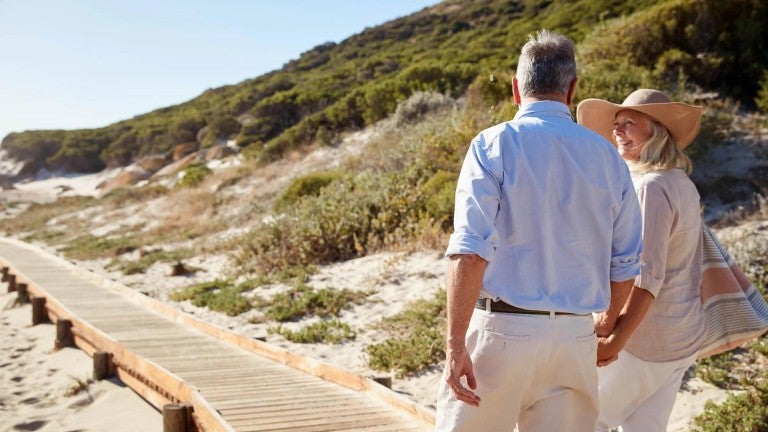 Older couple walking on sidewalk on beach.