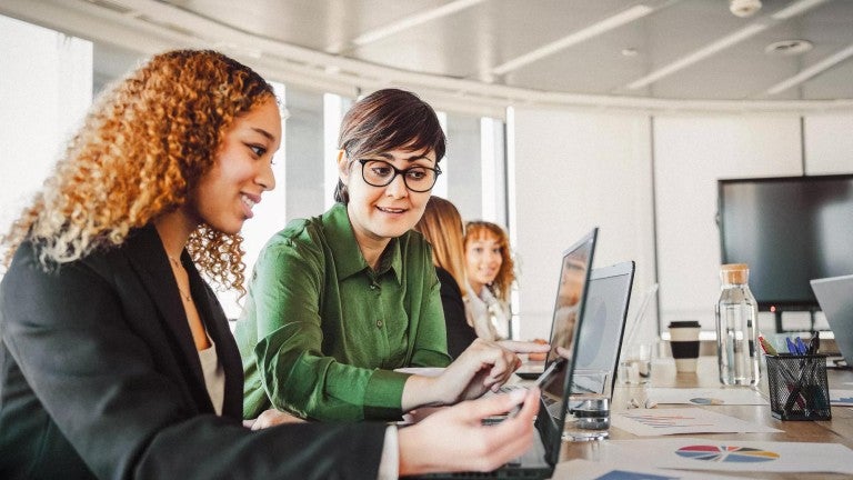 Two women sitting next to each other looking at a computer screen.