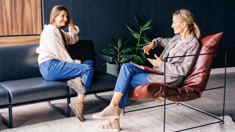 Two women seated in office space having a conversation.