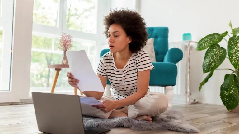 Young woman sitting on a rug on the floor looking at her computer