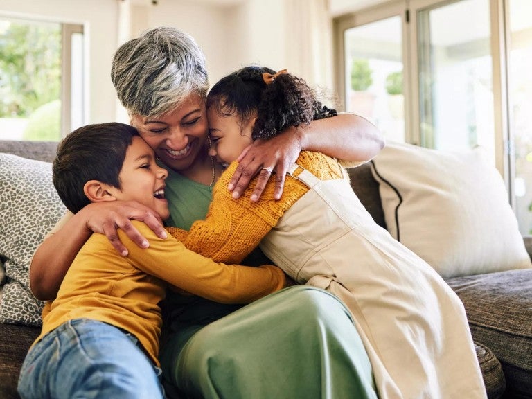 A grandmother hugging her grandchildren indoors.
