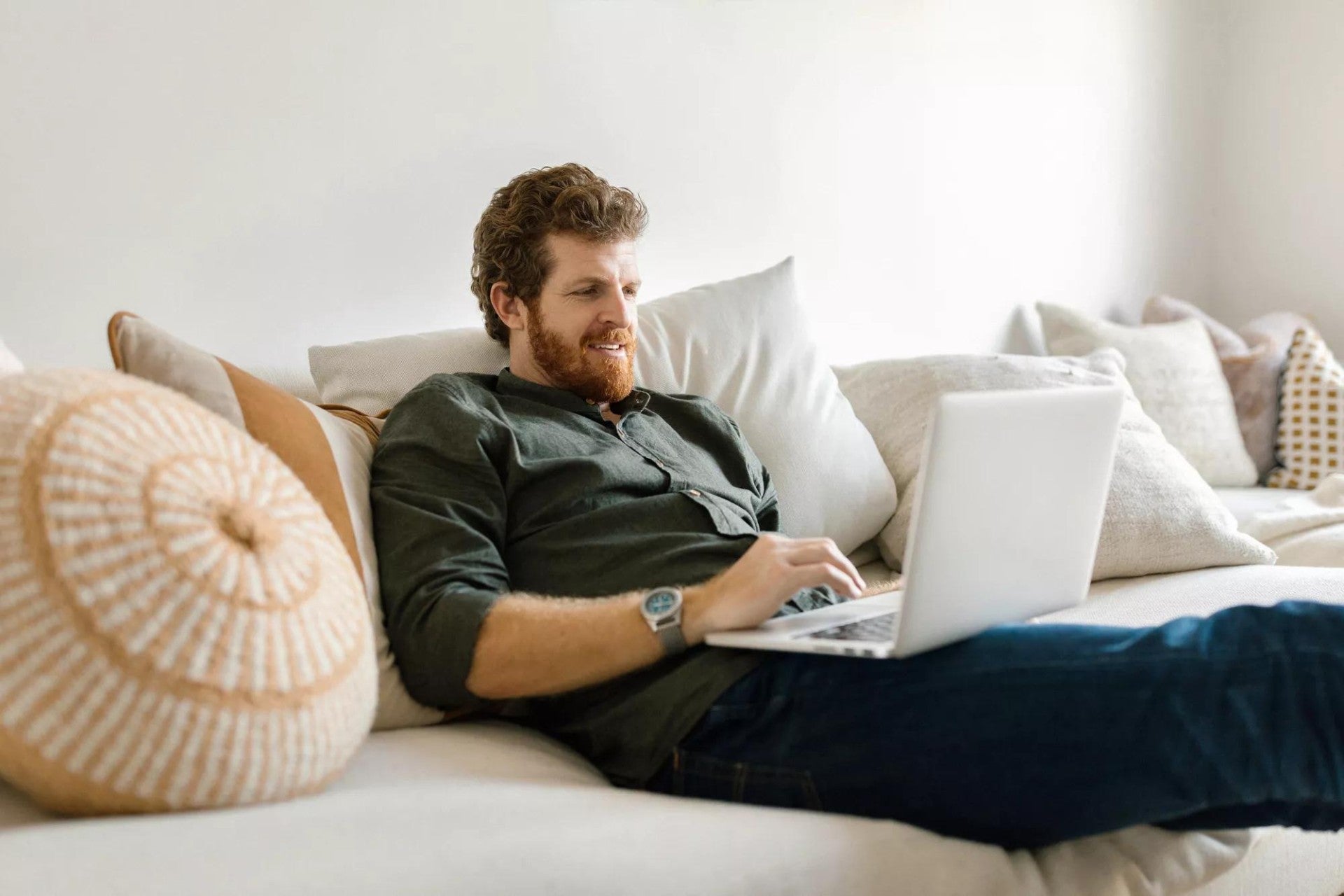 Man sitting on a tan couch working on a laptop.