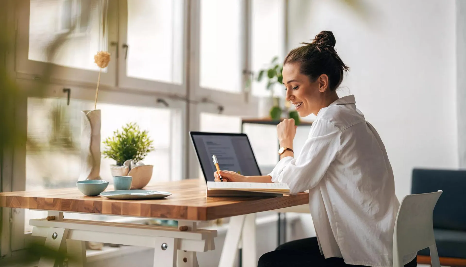 A young woman in a white shirt working on a laptop at a desk.