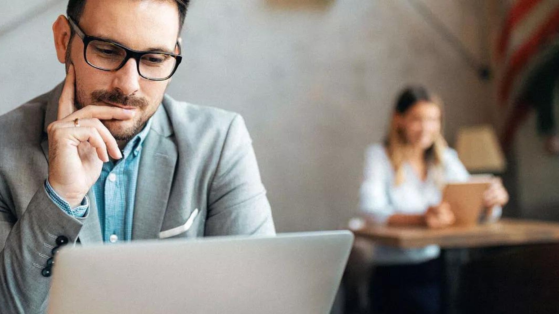 Picture of a man in a suit casually looking at his laptop.
