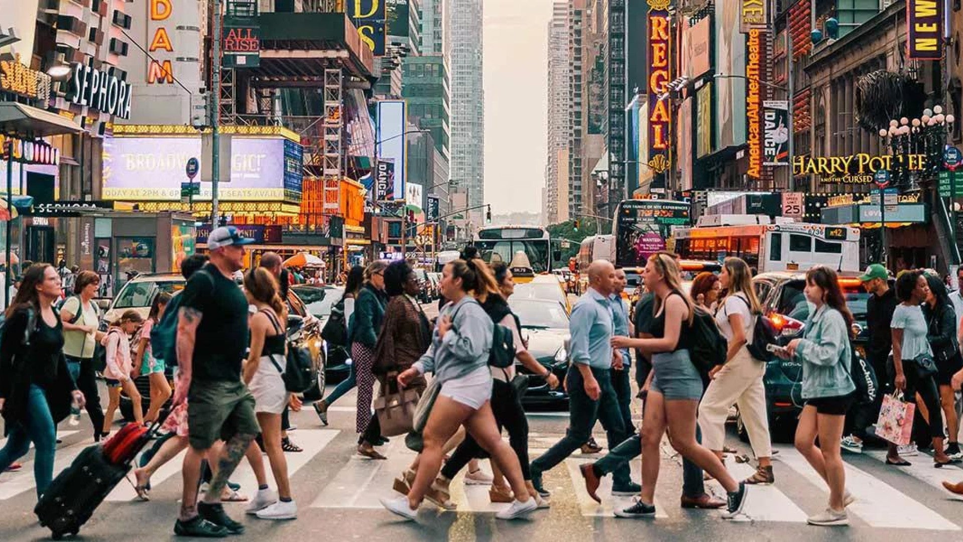 Photo of dozens of people walking across a crowded crosswalk at a busy city intersection.