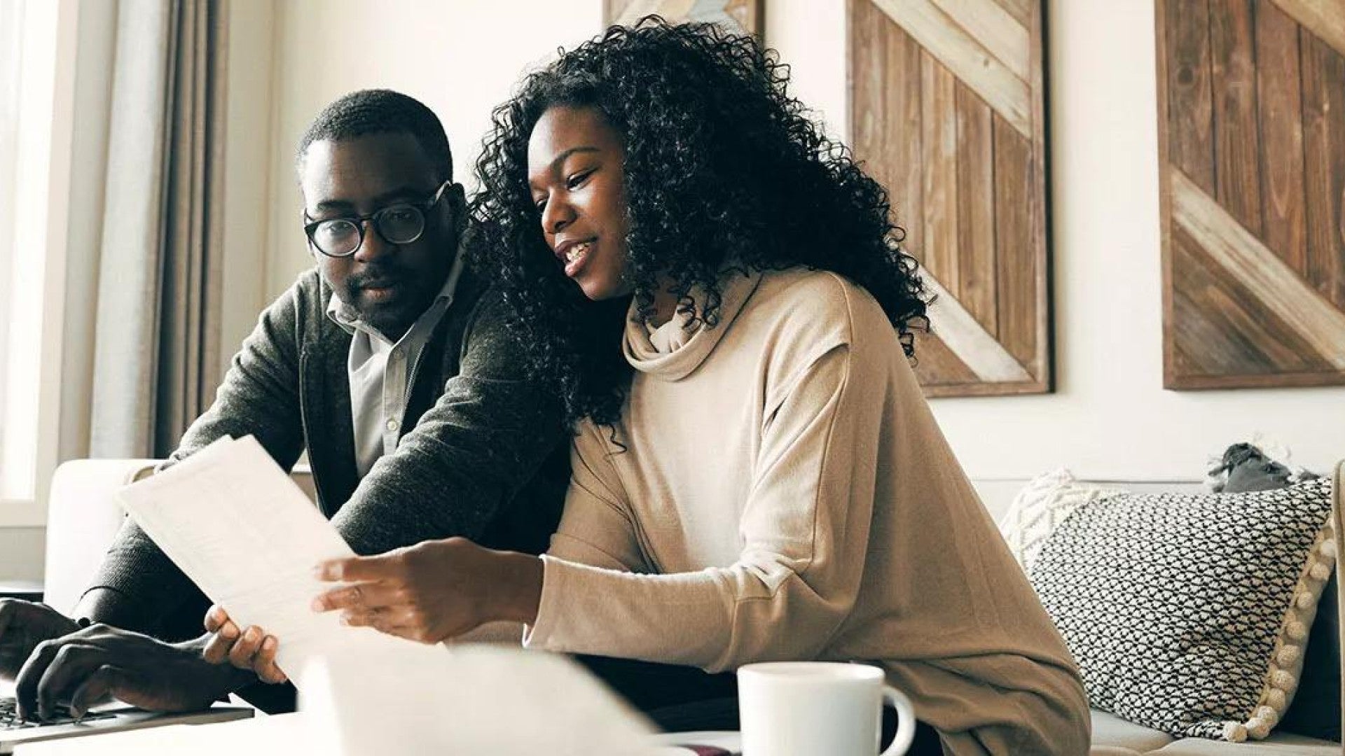 A couple sitting on the couch in their living room reviewing documents related to their investments.