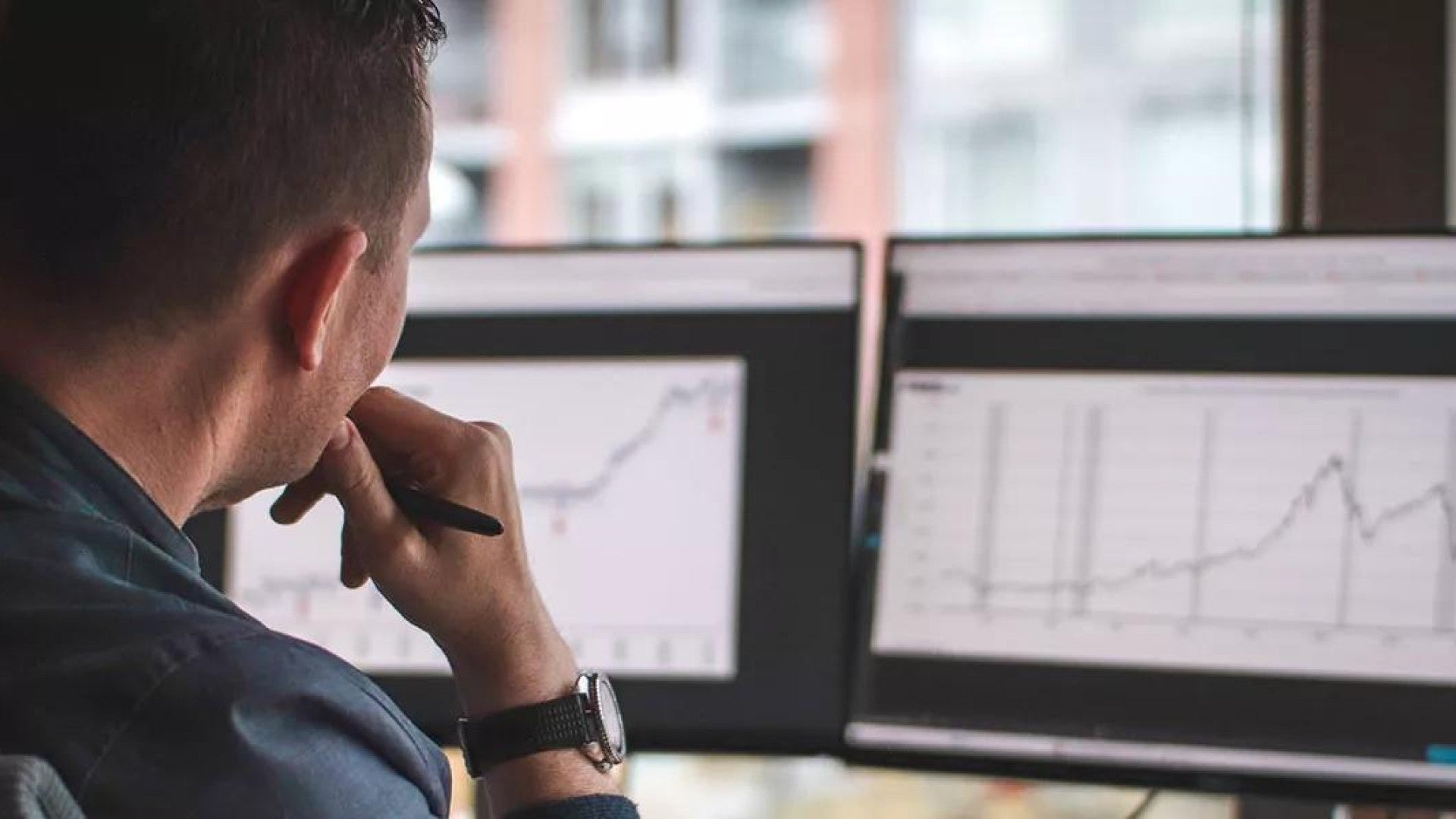 Photo of a man looking at two computer monitors.