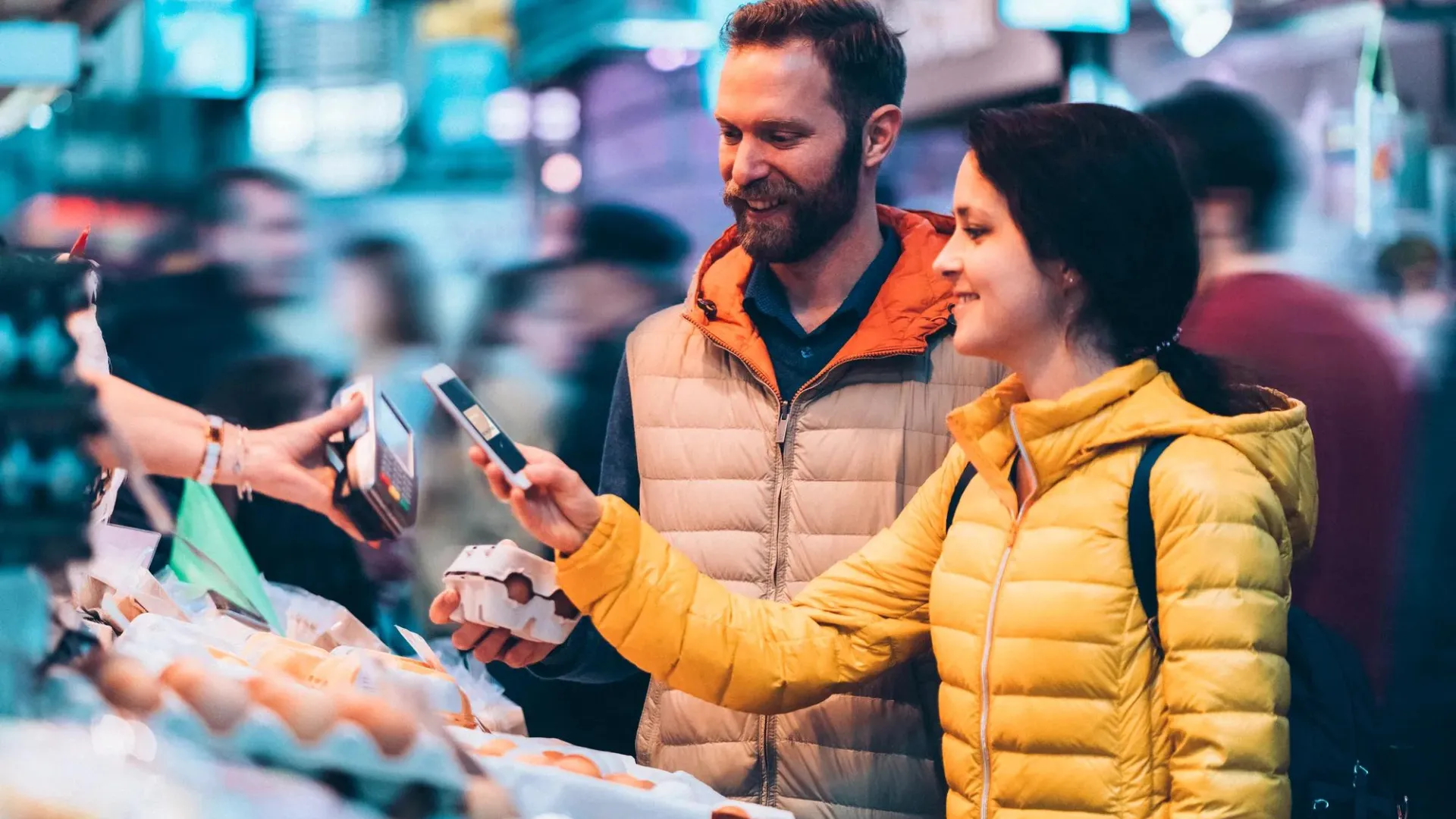 Young couple buying eggs on the street market using tap to pay.