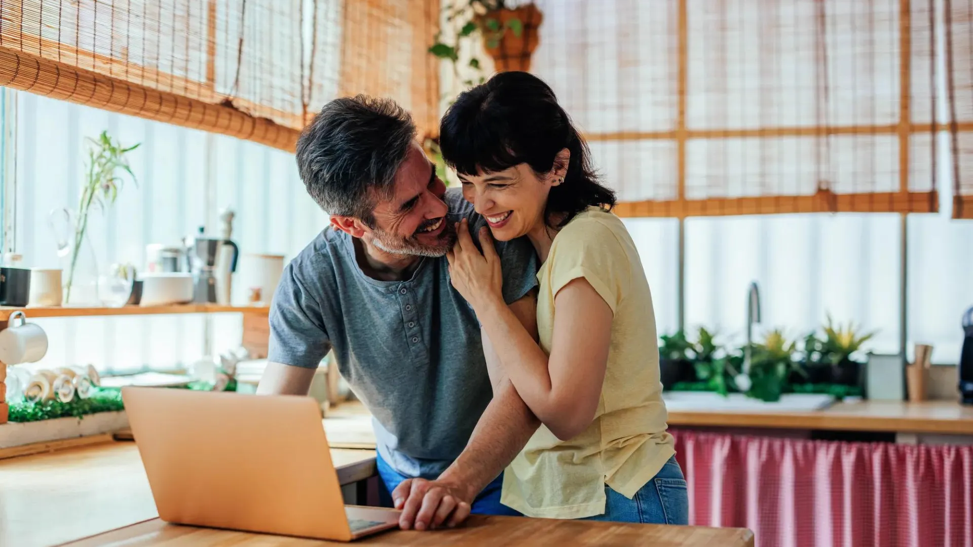 Couple standing together in a kitchen looking at a computer.