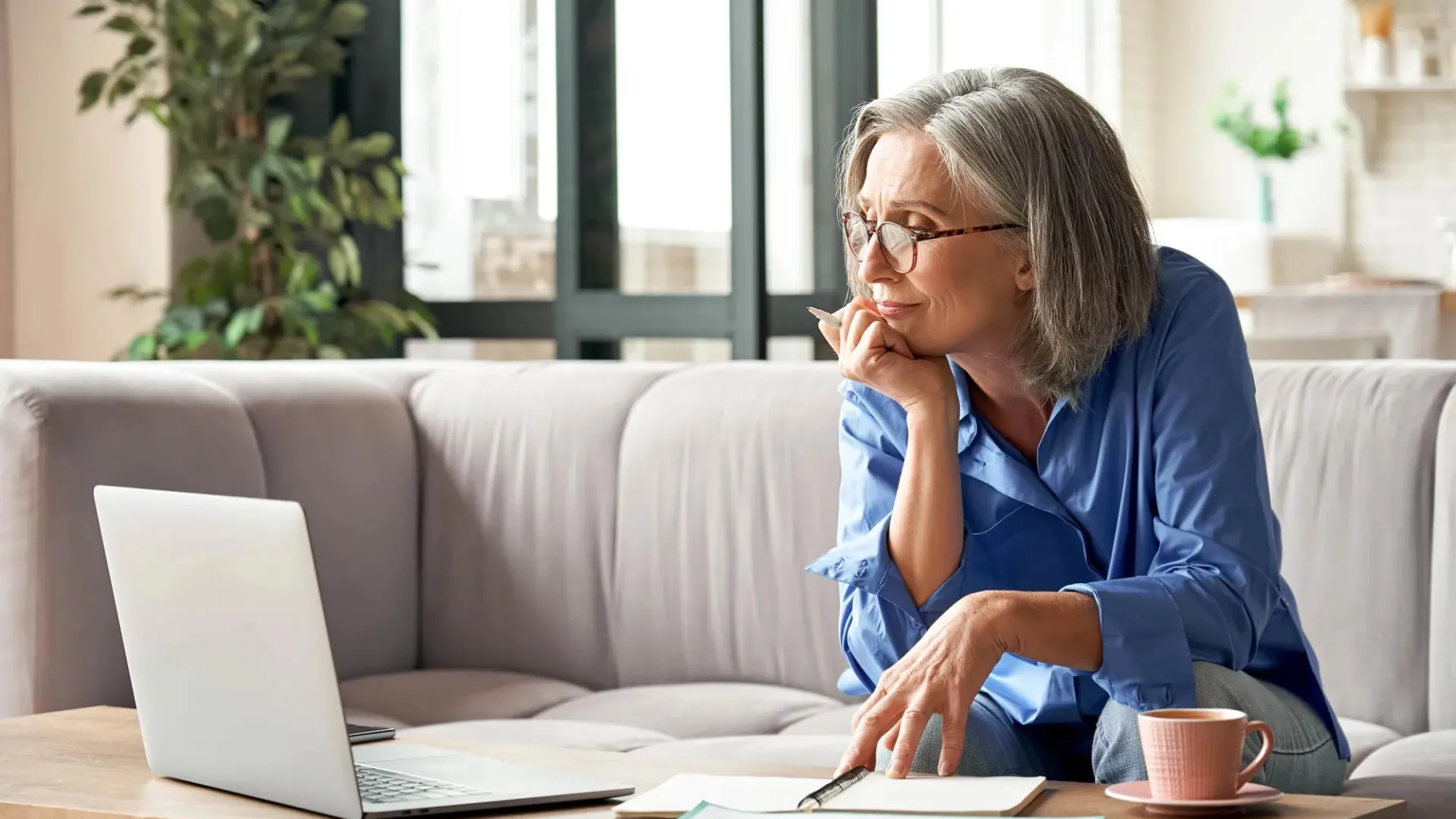 Woman in her living room resting her chin on her hand as she looks at her laptop.