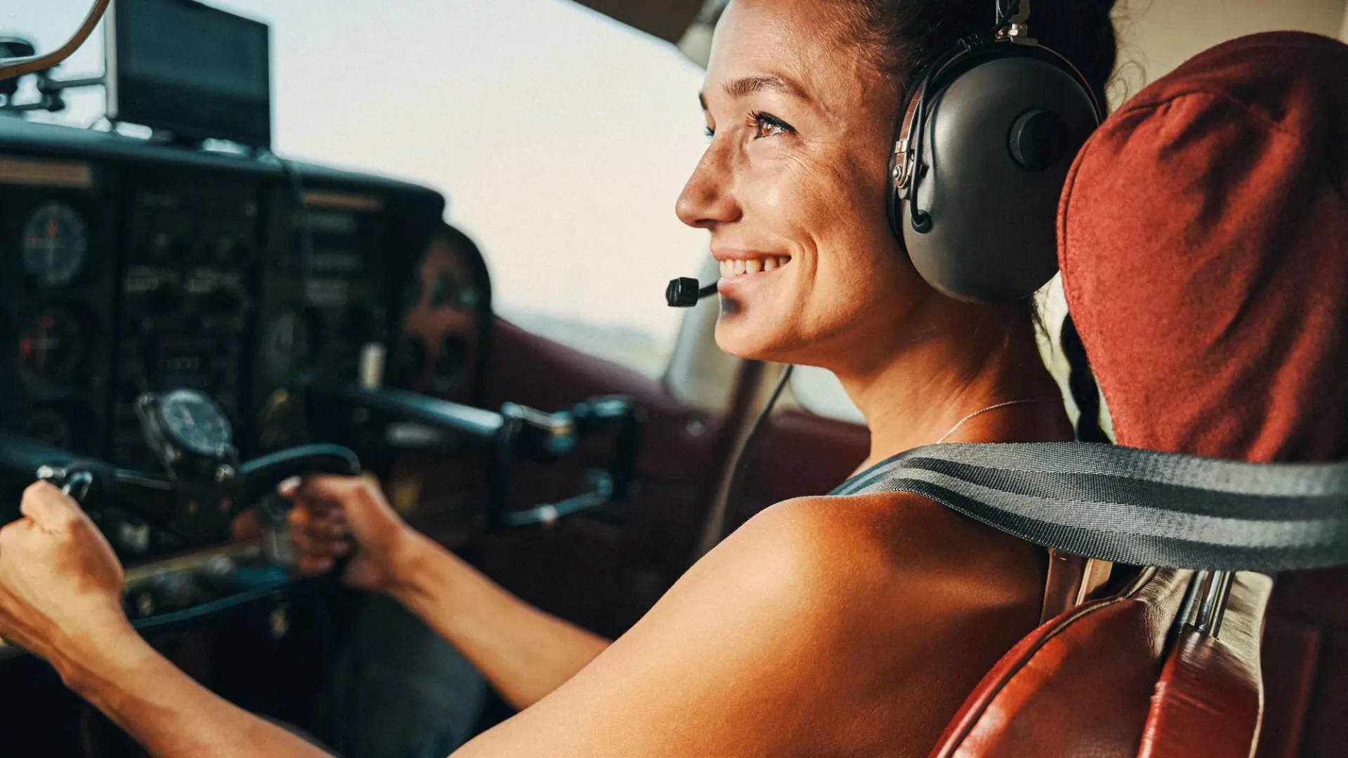 Woman piloting a small aircraft wearing a headset and big smile.