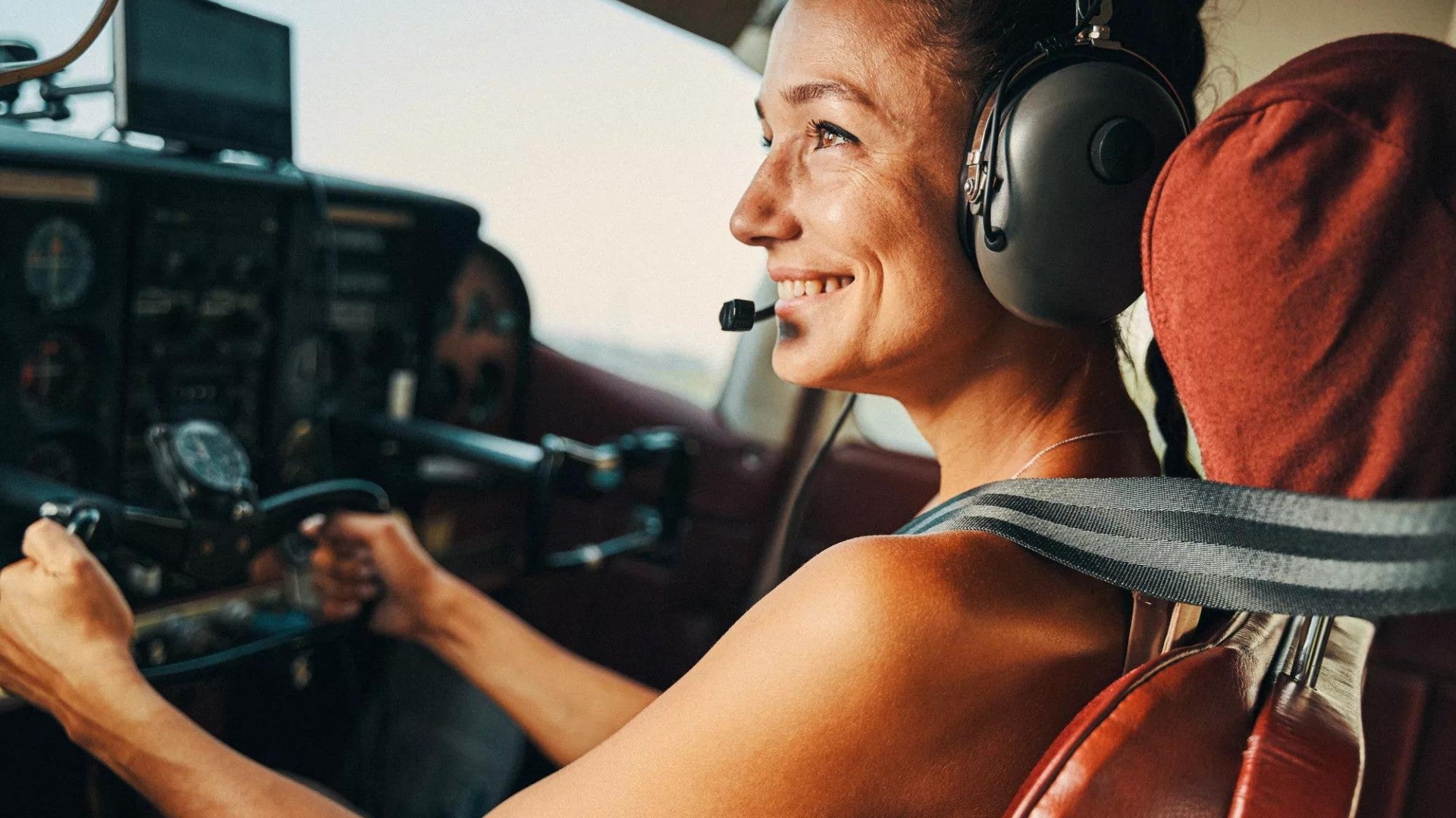 Woman piloting a small aircraft wearing a headset and big smile.