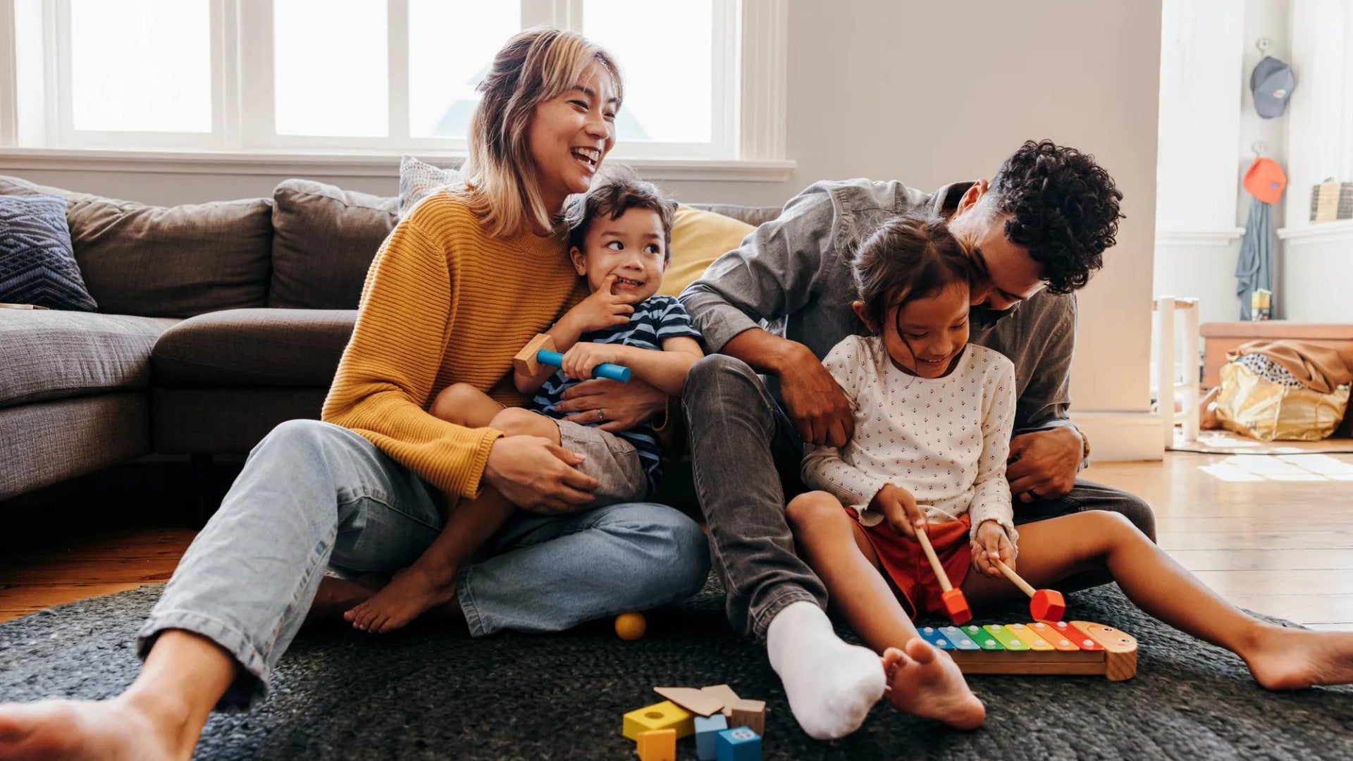 Family of four sitting on rug in living room playing and laughing