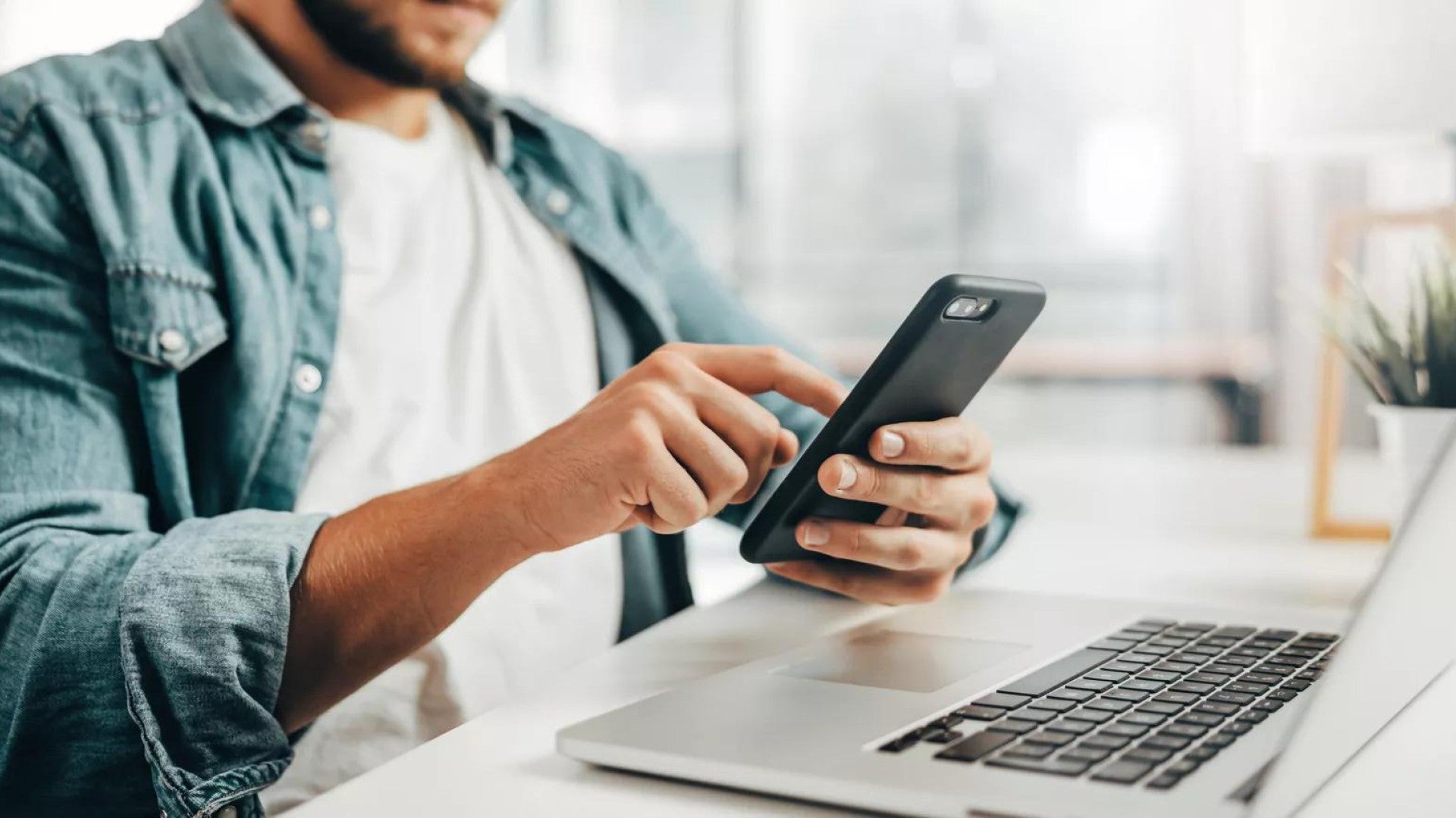 Un hombre revisando su teléfono y computadora