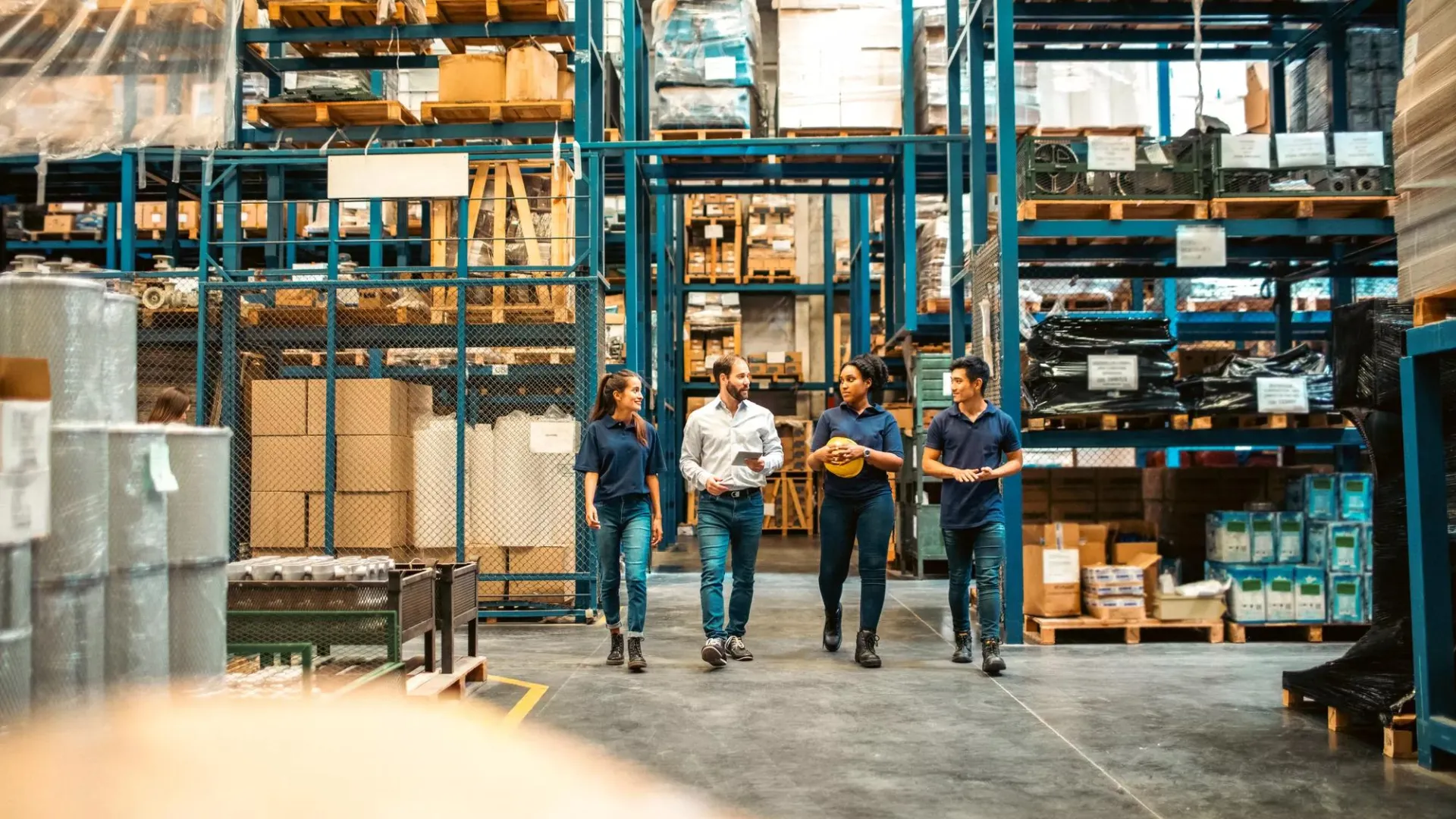 A group of four warehouse employees walking through an aisle of storage racks and talking