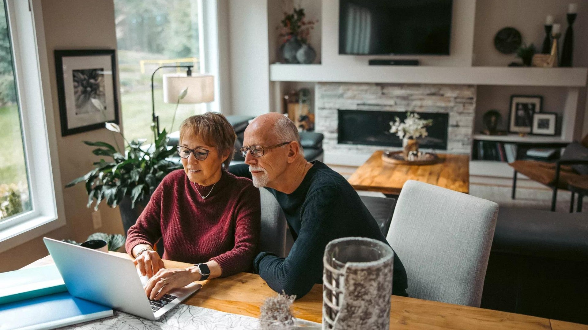 Older couple working together on laptop from dining room table.