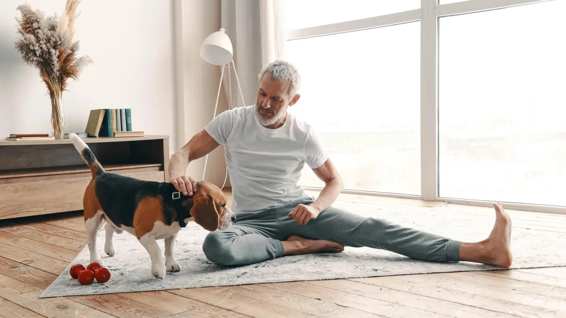 Man sitting on floor, stretching, while petting his dog.