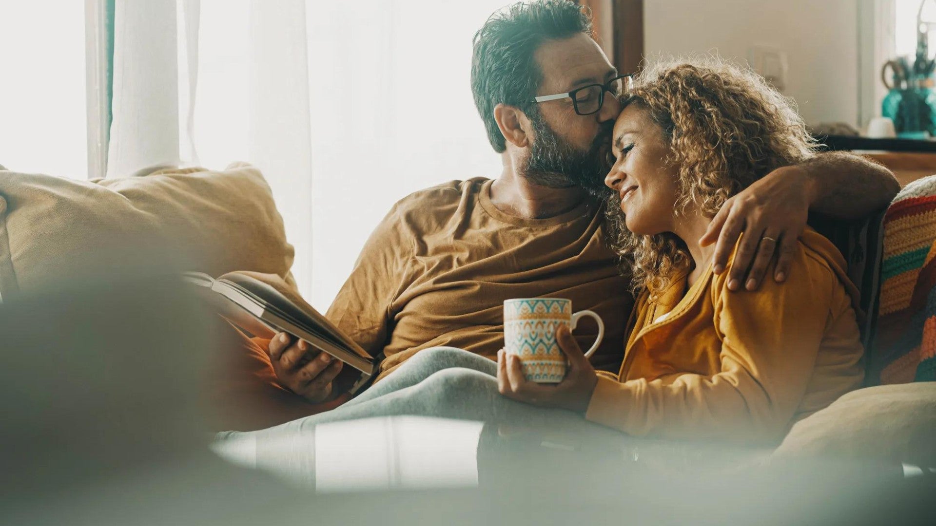 Couple relaxing on living room couch with coffee and a book.