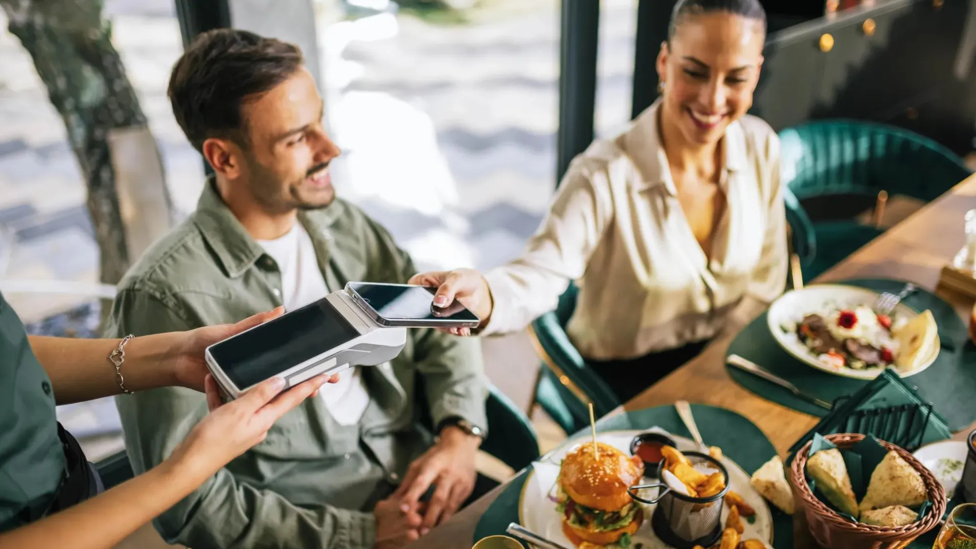 Mujer paga su comida con el teléfono móvil mientras sale a comer con amigos.