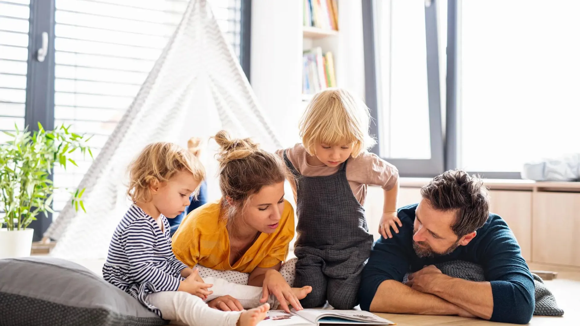Madre y padre jóvnes leyendo a sus hijos en su sala de estar.