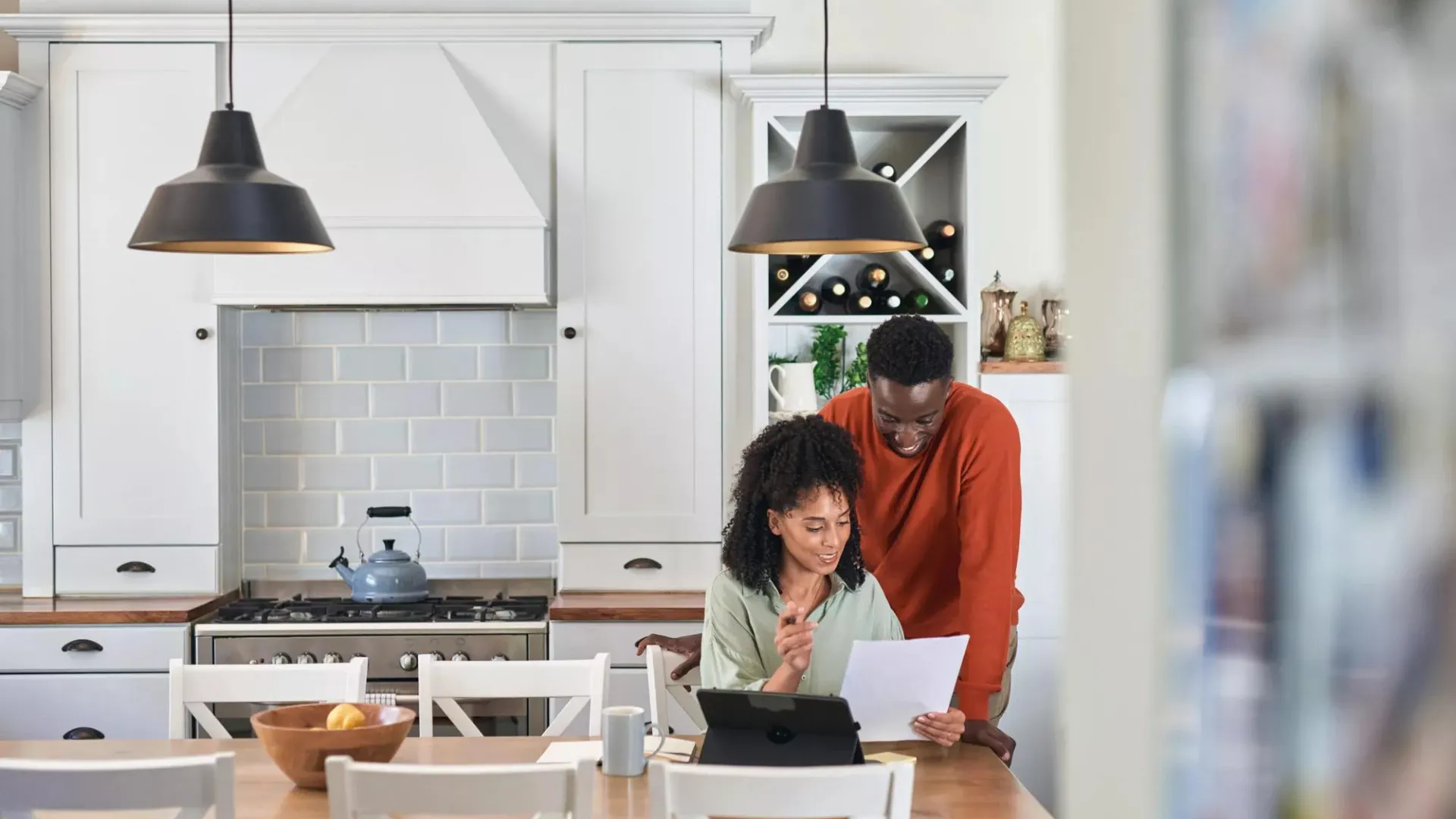 Una pareja joven en su cocina revisando documentos financieros. 
