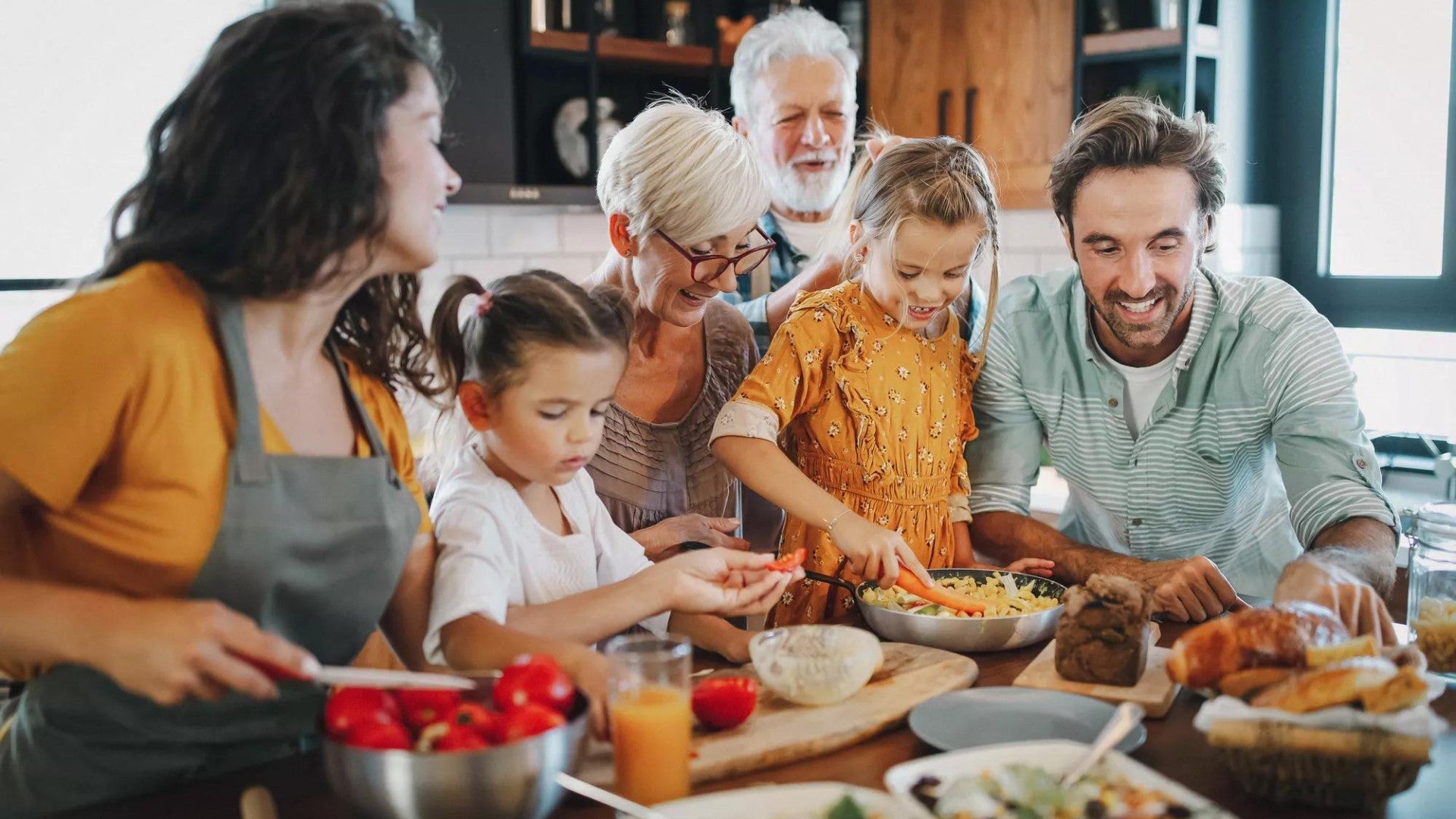 Parents, children, and grandchildren are gathered around a kitchen island making dinner together.