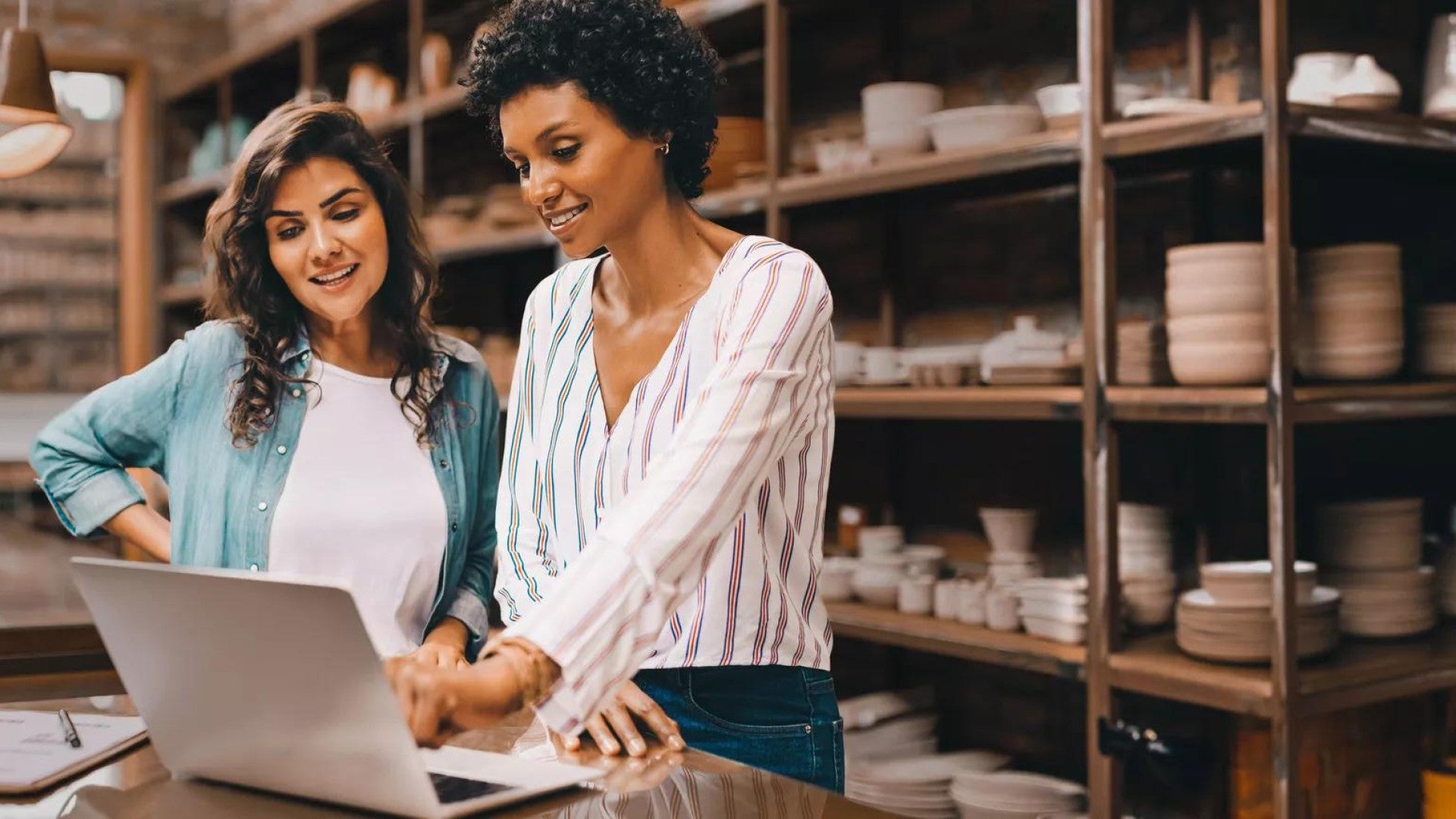 Young female ceramists using a laptop together in their store.