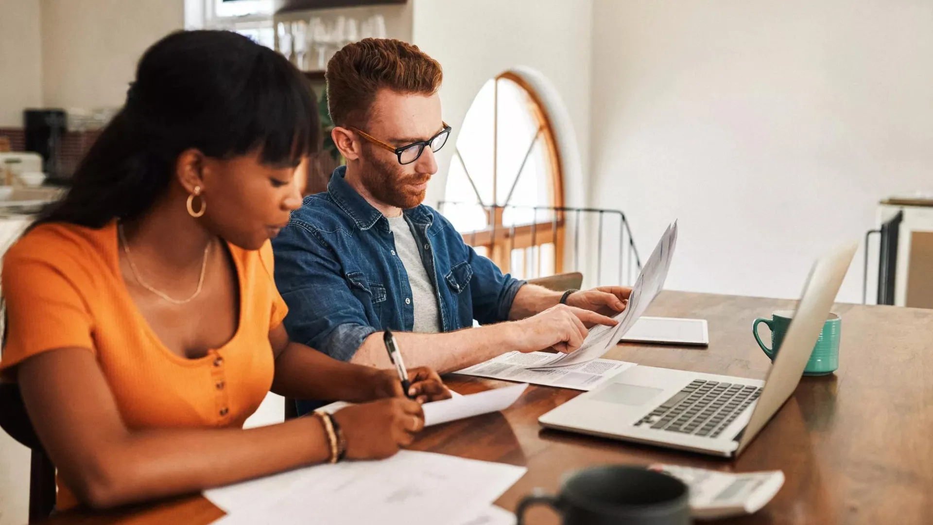 Couple looking at paperwork while sitting with their laptop.