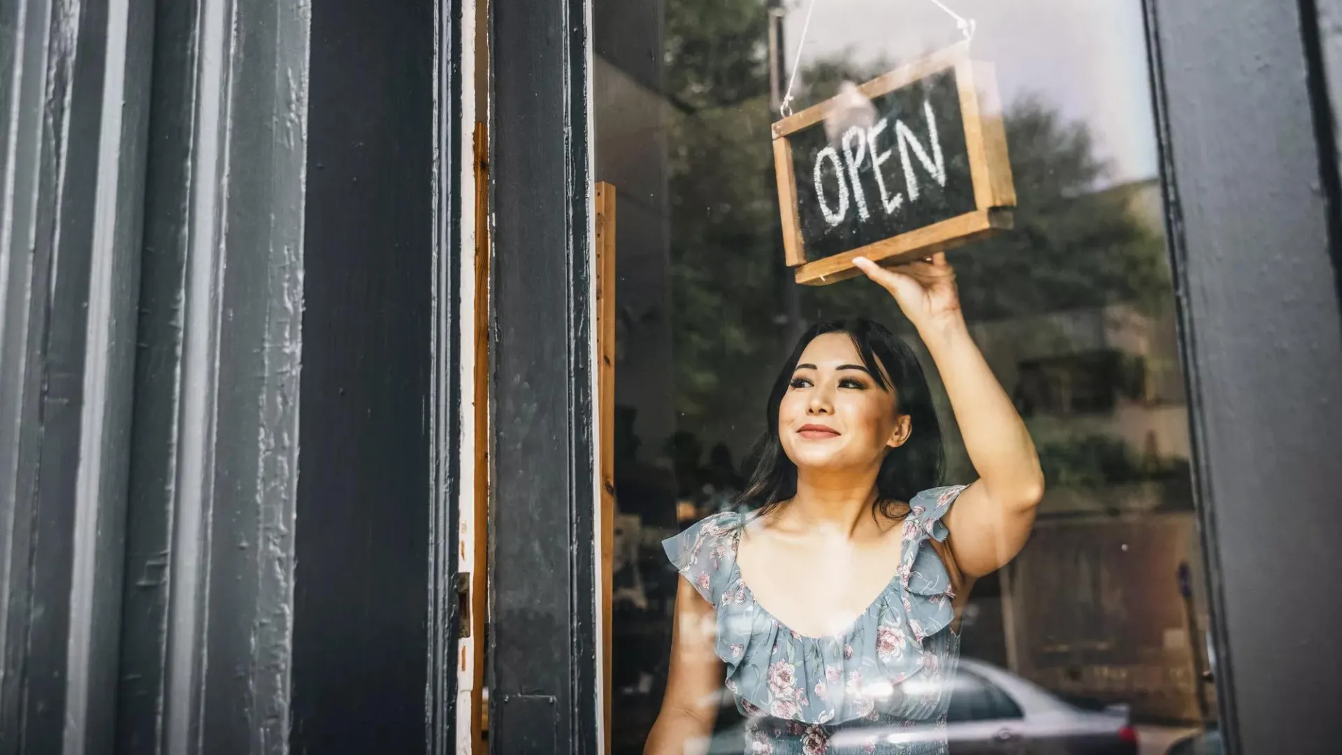 A woman turning the open sign on the front door of a small business.