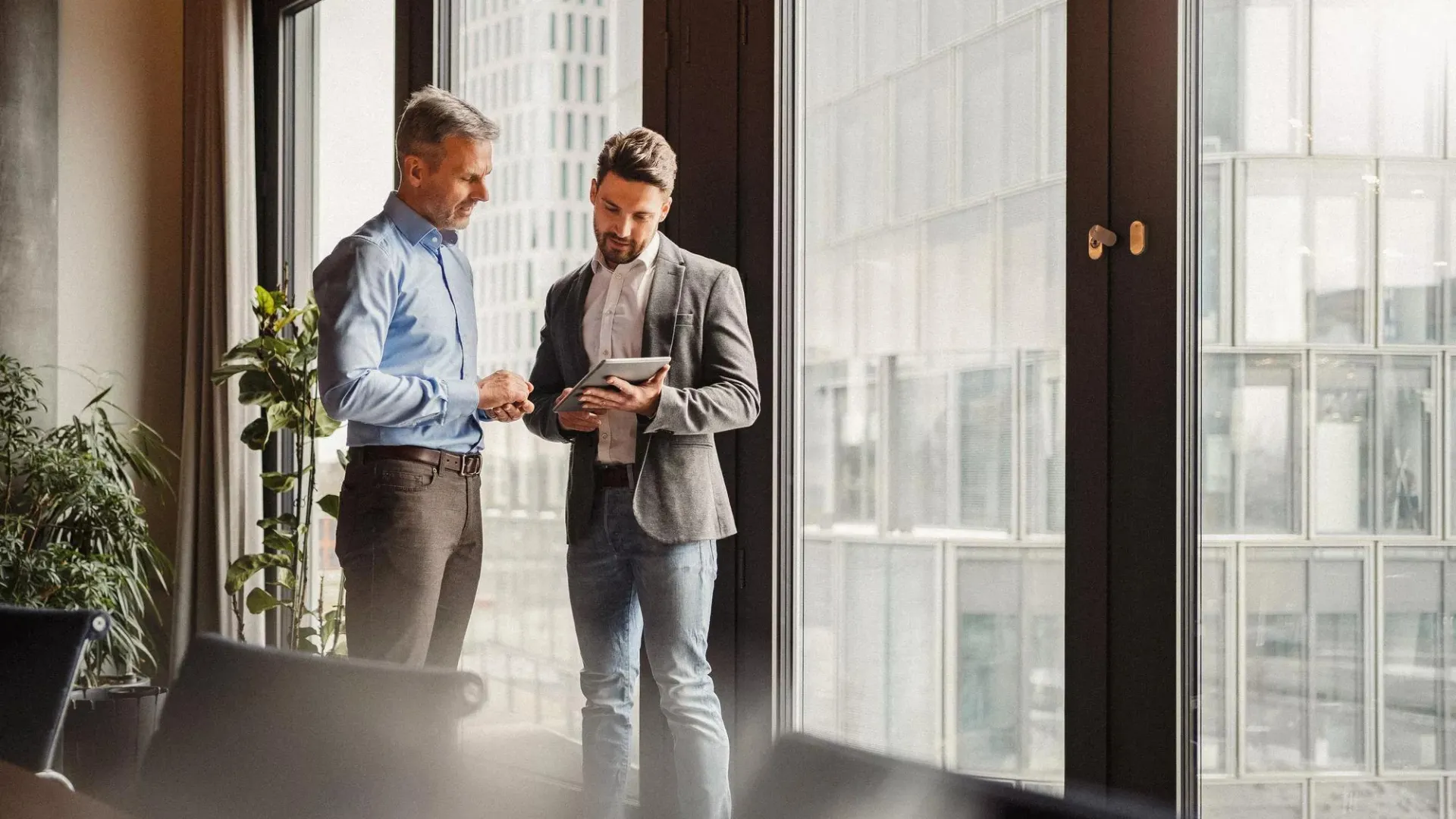 Two men standing in a conference room looking at a tablet computer.