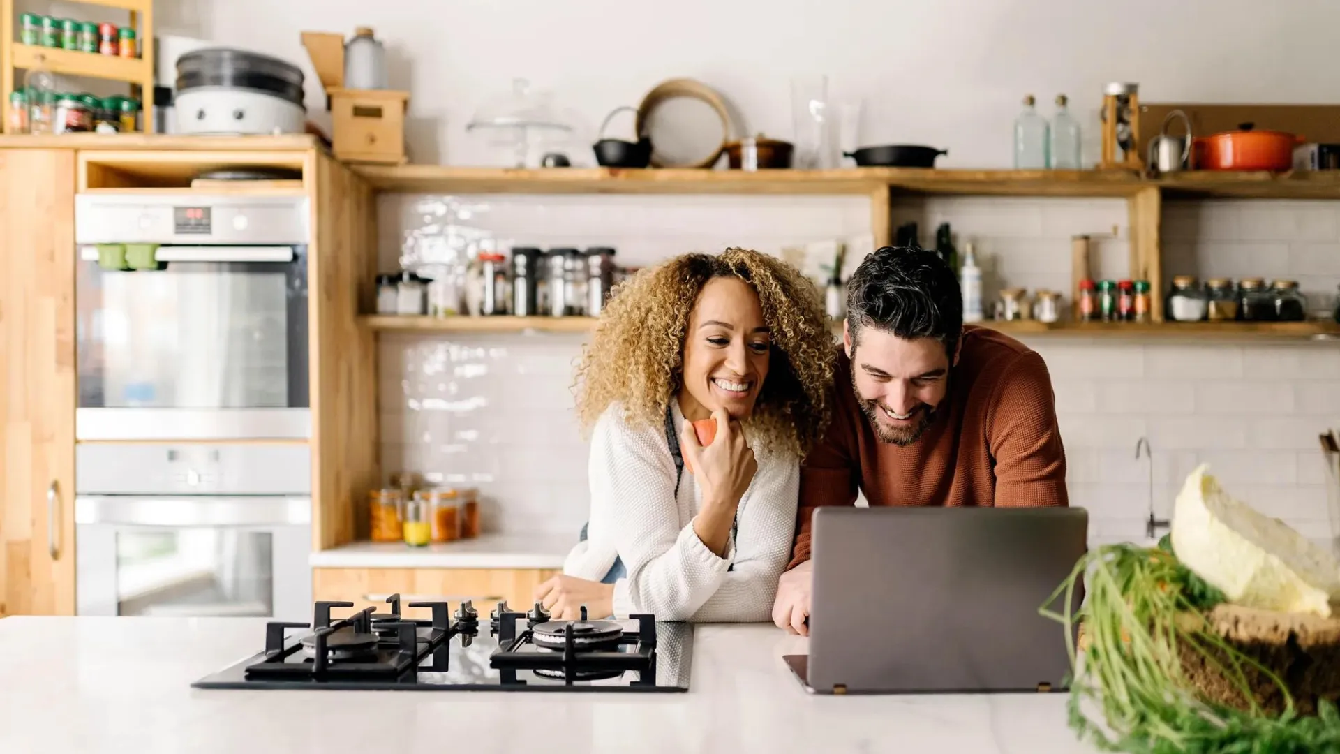 Man & woman in kitchen looking at financial information on a laptop