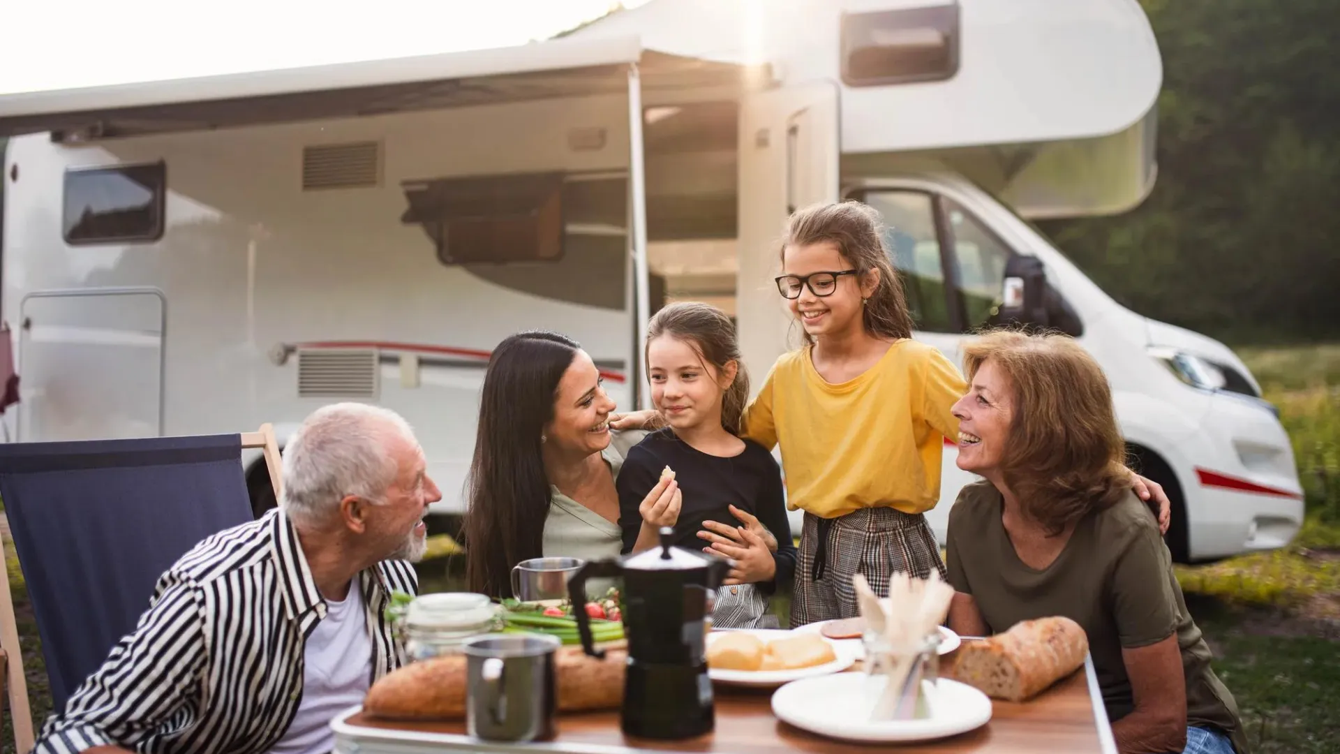 Grandparents, mom, and two daughters eating at table outside with RV in background