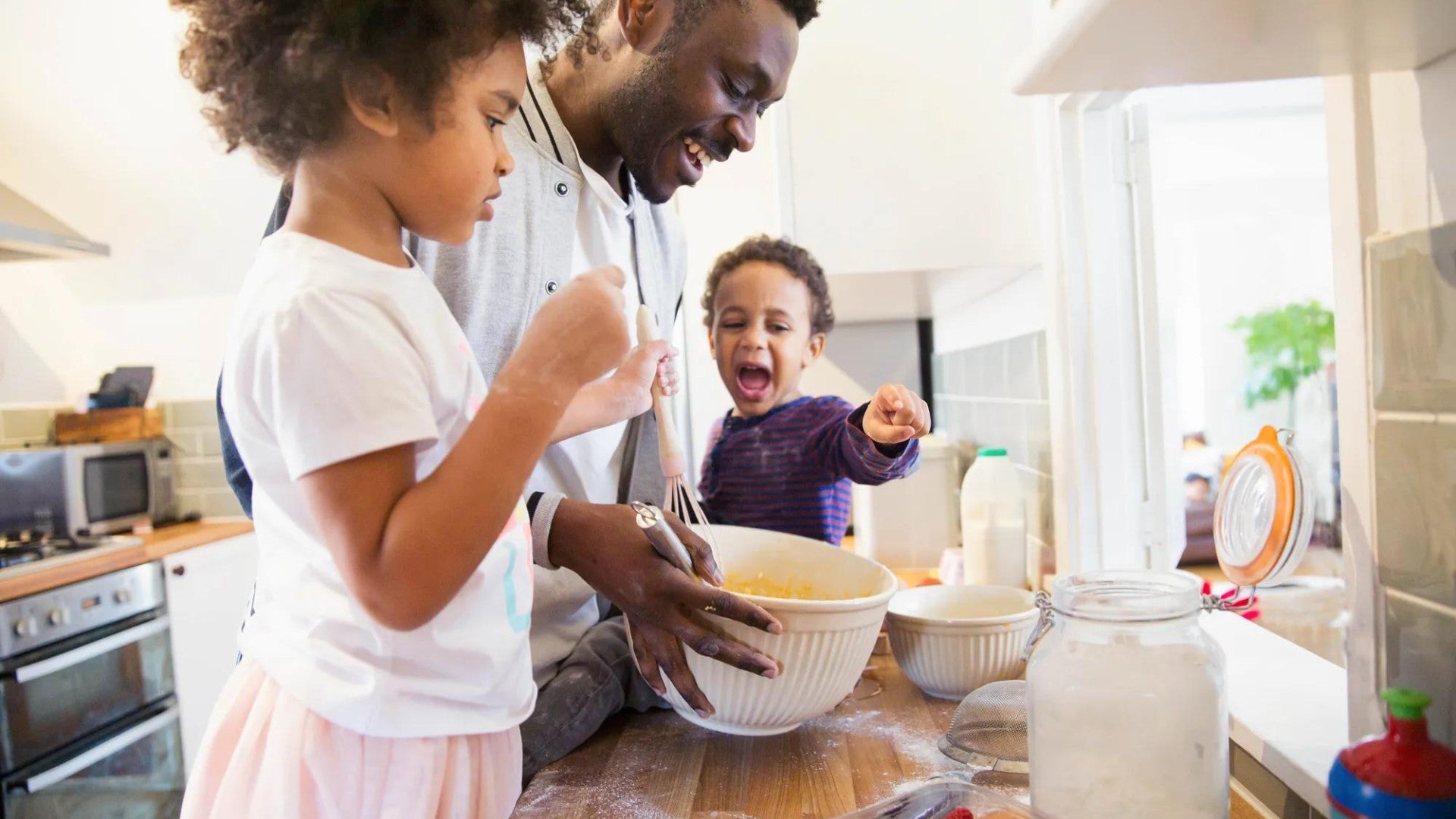 Family baking together in kitchen - adult and two children mixing ingredients in bowls on counter