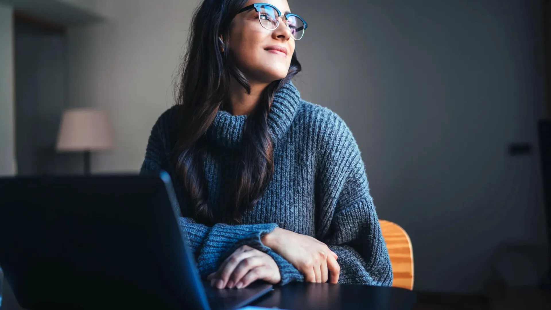 A woman seated behind a laptop in a home office.