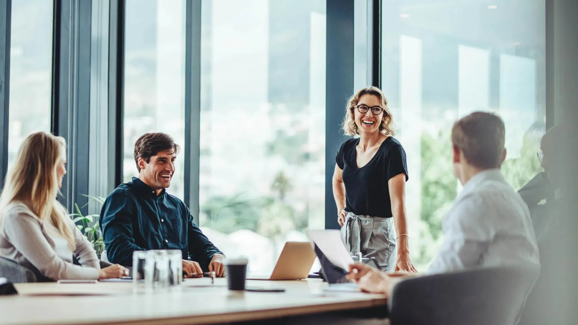 our employees, one of whom is standing, around a desk smiling and discussing business.