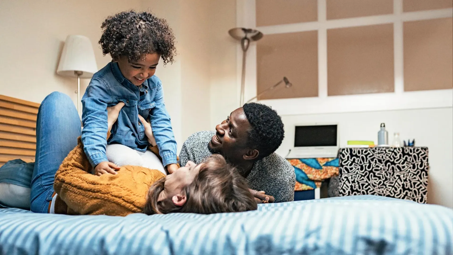A joyful family moment as parents and child play together on a bed, laughing and being playful in a casual home setting.